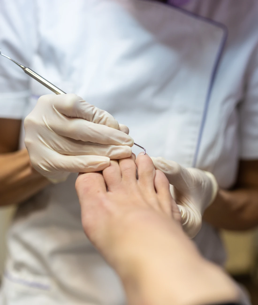 Fußpflegebehandlung durch Podologin mit Werkzeug und Handschuhen.